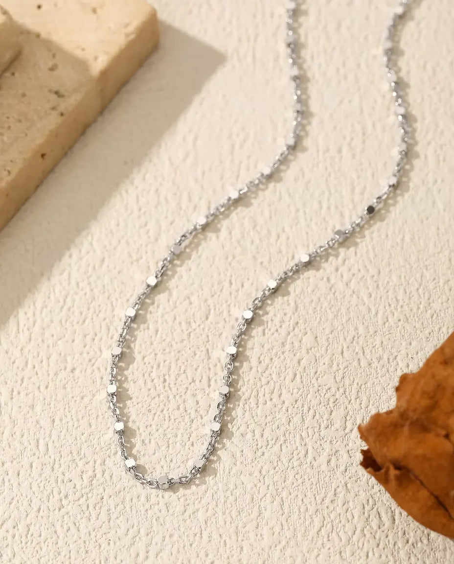 Sequin Chain Necklace in 925 Sterling Silver - draped across a cream surface beside a travertine slab