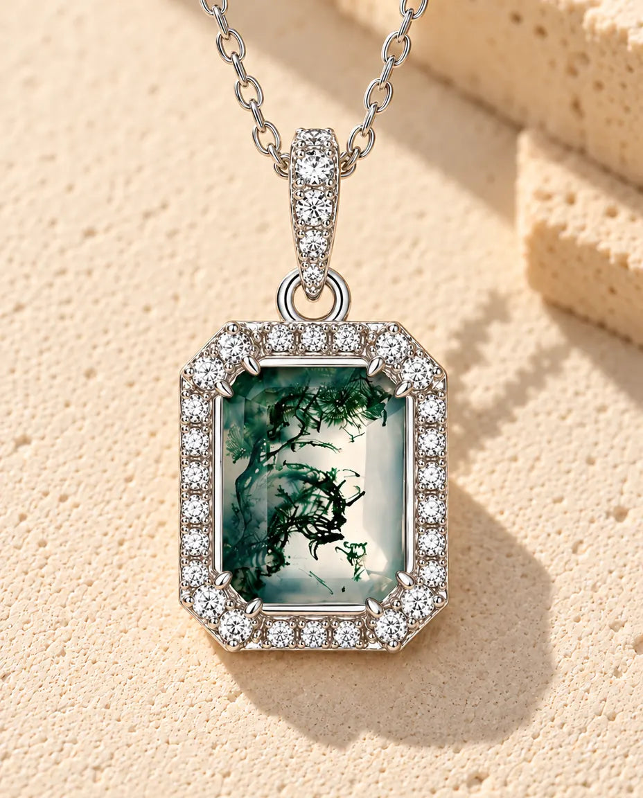 Emerald Cut Moss Agate Halo Necklace in 925 Sterling Silver - lying on a cream textured surface beside a travertine block
