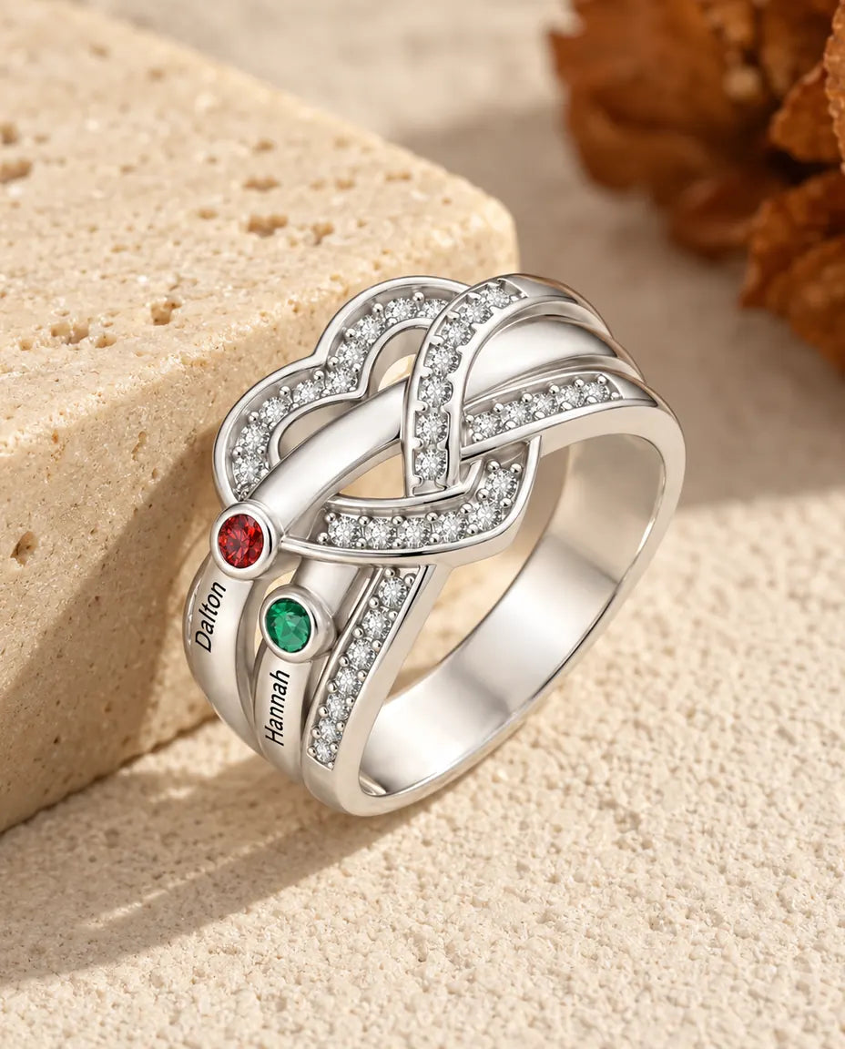 personalised heart knot birthstone ring with 2 names and 2 round birthstones, rhodium plated, on travertine