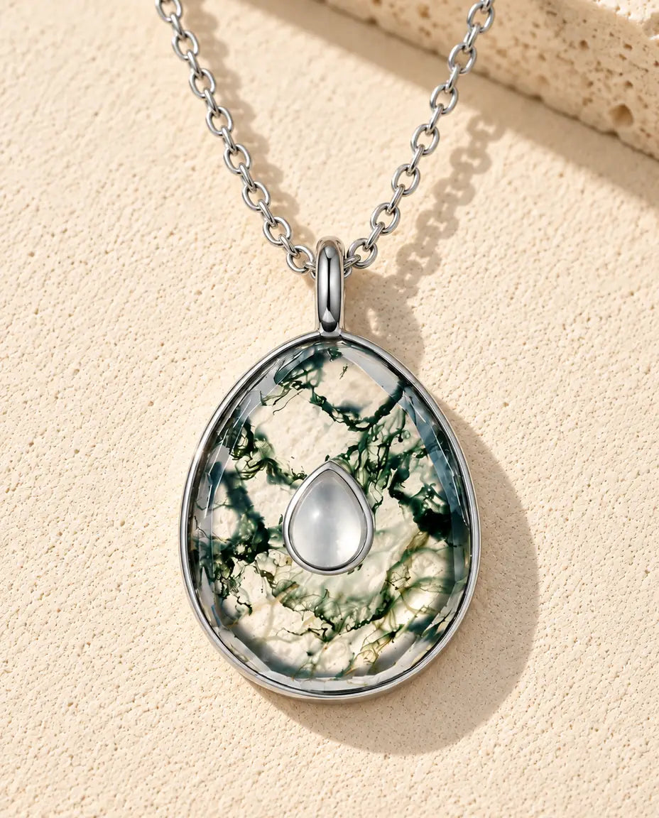Moss Agate Egg Pendant Necklace in 925 Sterling Silver - lying on a cream textured surface beside a travertine block