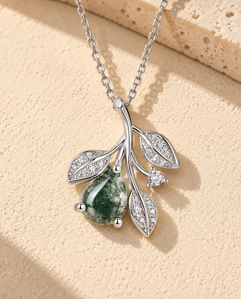 Moss Agate Leaf Necklace in 925 Sterling Silver - lying on a cream textured surface beside a travertine block