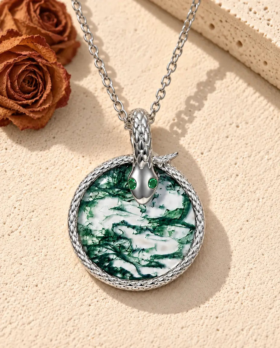 Moss Agate Snake Necklace in 925 Sterling Silver - lying on a cream textured surface beside a travertine block