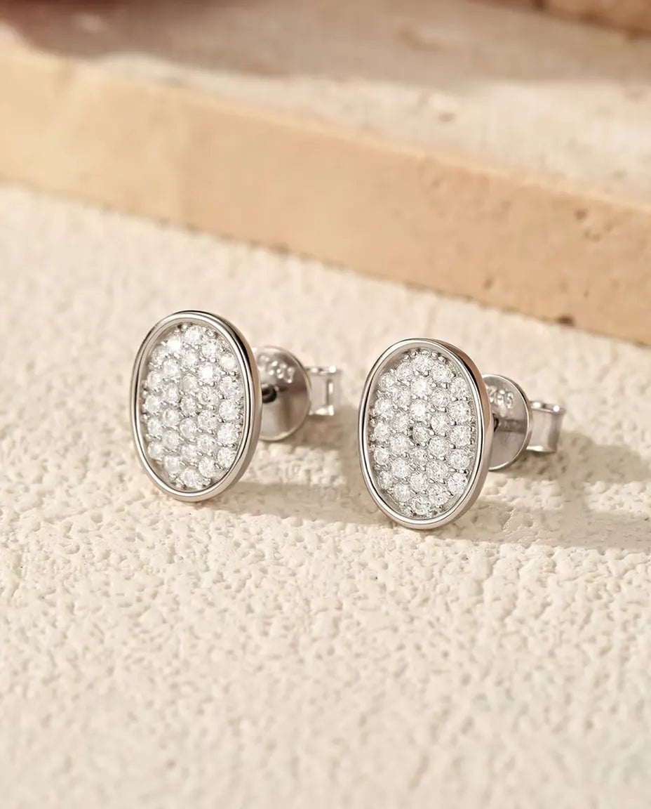 Oval Pave Moissanite Stud Earrings in 925 Sterling Silver - the pair lying on a cream textured surface