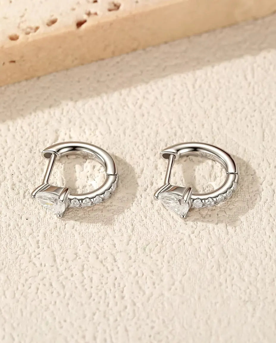 Pear Moissanite Huggie Hoop Earrings in 925 Sterling Silver - the pair lying on a cream textured surface
