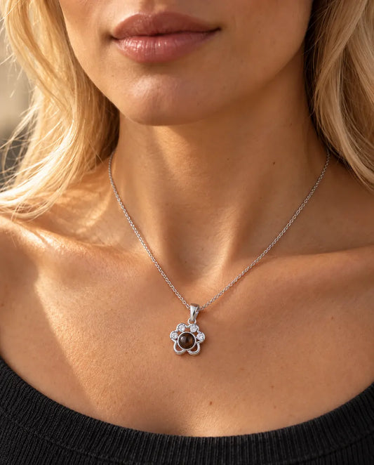 Woman in a charcoal knit top wearing the silver tone paw print projection necklace