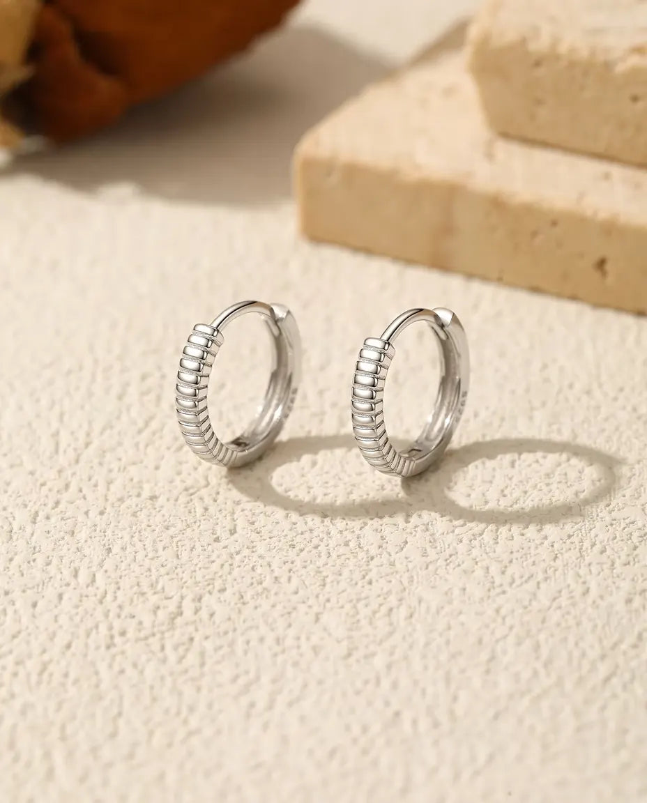 Ribbed Huggie Hoop Earrings in 925 Sterling Silver - pair standing side by side on a cream textured surface