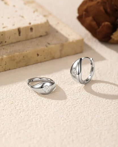 Asscher Cut Moissanite Huggie Hoop Earrings in 925 Sterling Silver - pair on a cream textured surface, one lying flat and one standing