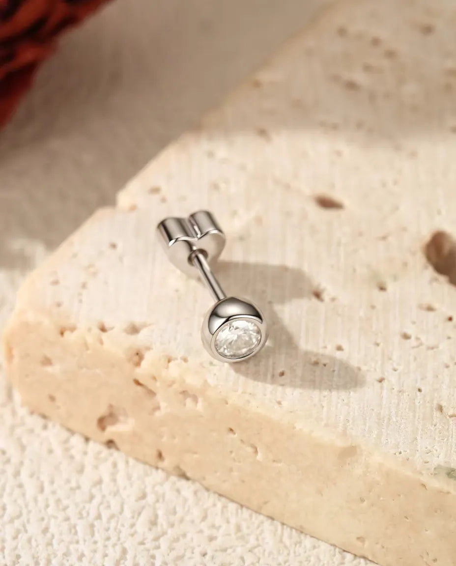 Bezel Moissanite Stud Earrings in 925 Sterling Silver - lying on a cream textured surface beside a travertine slab