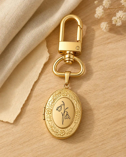 Gold birth flower photo locket keyring engraved with a snowdrop on a wood table