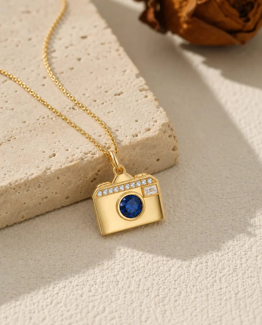 Gold camera photo locket necklace with a blue birthstone lens