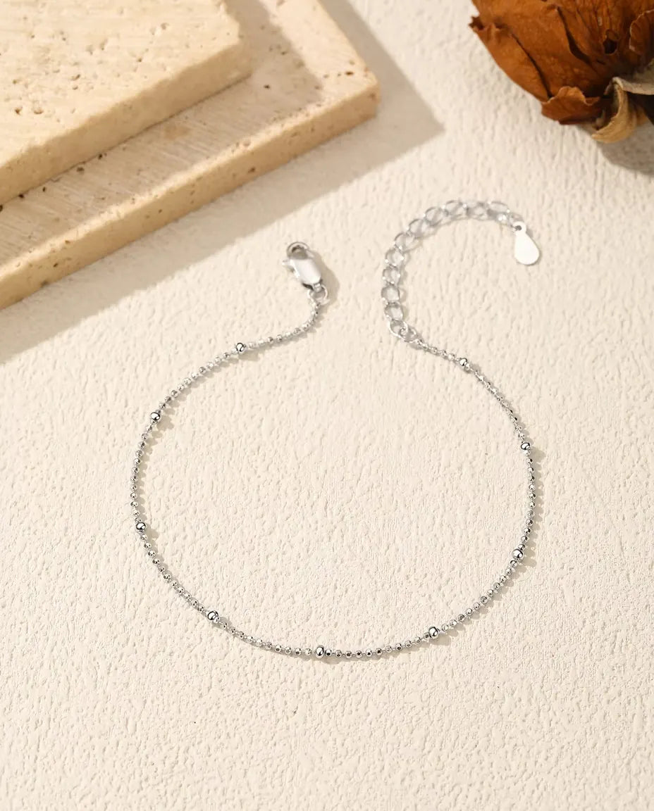 Bead Chain Bracelet in 925 Sterling Silver - laid flat on a cream textured surface with the clasp and extender