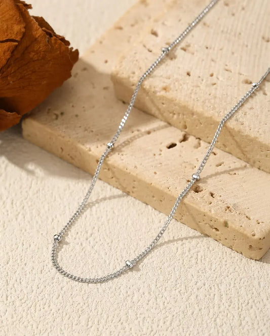 Satellite Chain Necklace in 925 Sterling Silver - draped across a cream surface beside a travertine slab