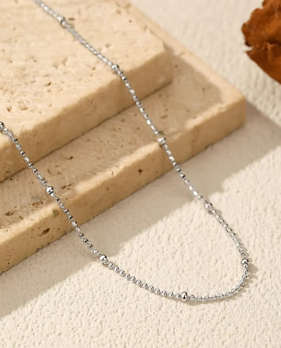 Bead Chain Necklace in 925 Sterling Silver - draped across a cream surface beside a travertine slab