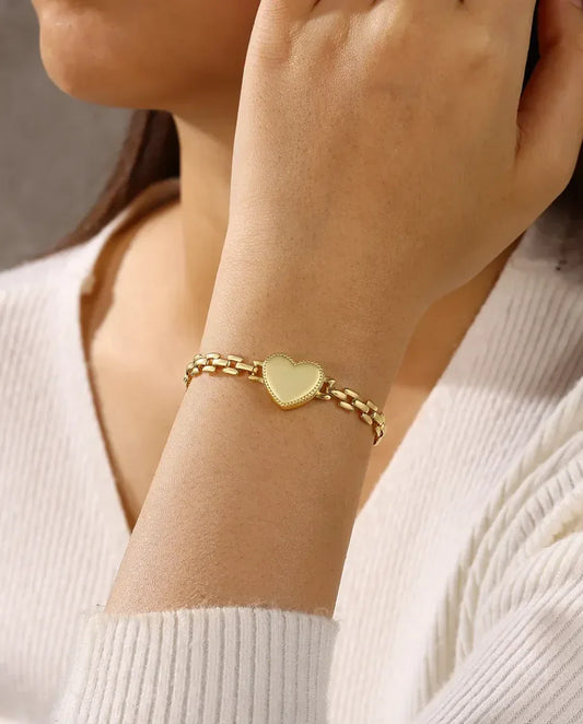 Woman wearing gold heart charm bracelet with white knit sweater