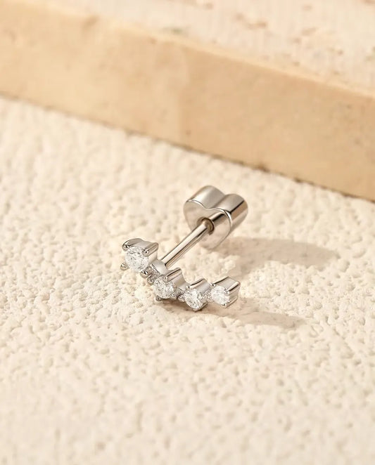 Curved Moissanite Climber Stud Earrings in 925 Sterling Silver - lying on a cream textured surface beside a travertine slab