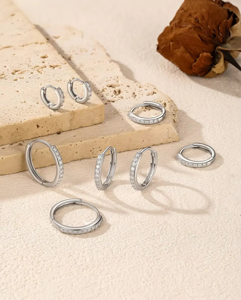 Moissanite Huggie Hoop Earrings in 925 Sterling Silver - five sizes spread over a travertine slab and a cream surface