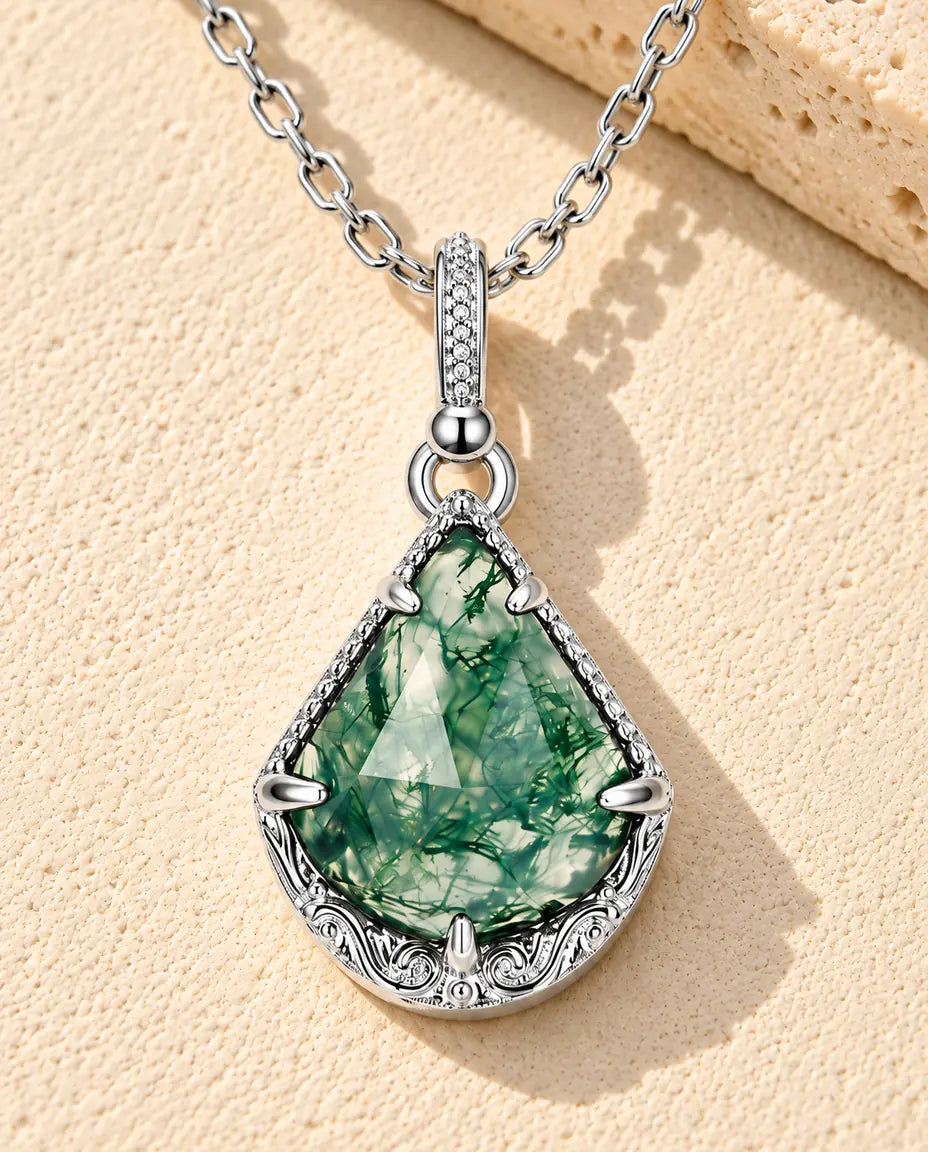 Moss Agate Shield Necklace in 925 Sterling Silver - lying on a cream textured surface beside a travertine block