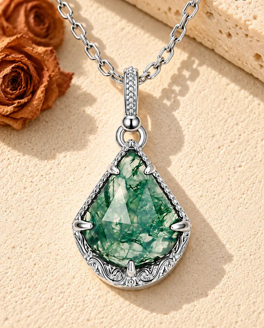 Moss Agate Shield Necklace in 925 Sterling Silver - lying on a cream textured surface beside a travertine block