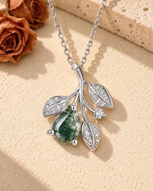 Moss Agate Leaf Necklace in 925 Sterling Silver - lying on a cream textured surface beside a travertine block