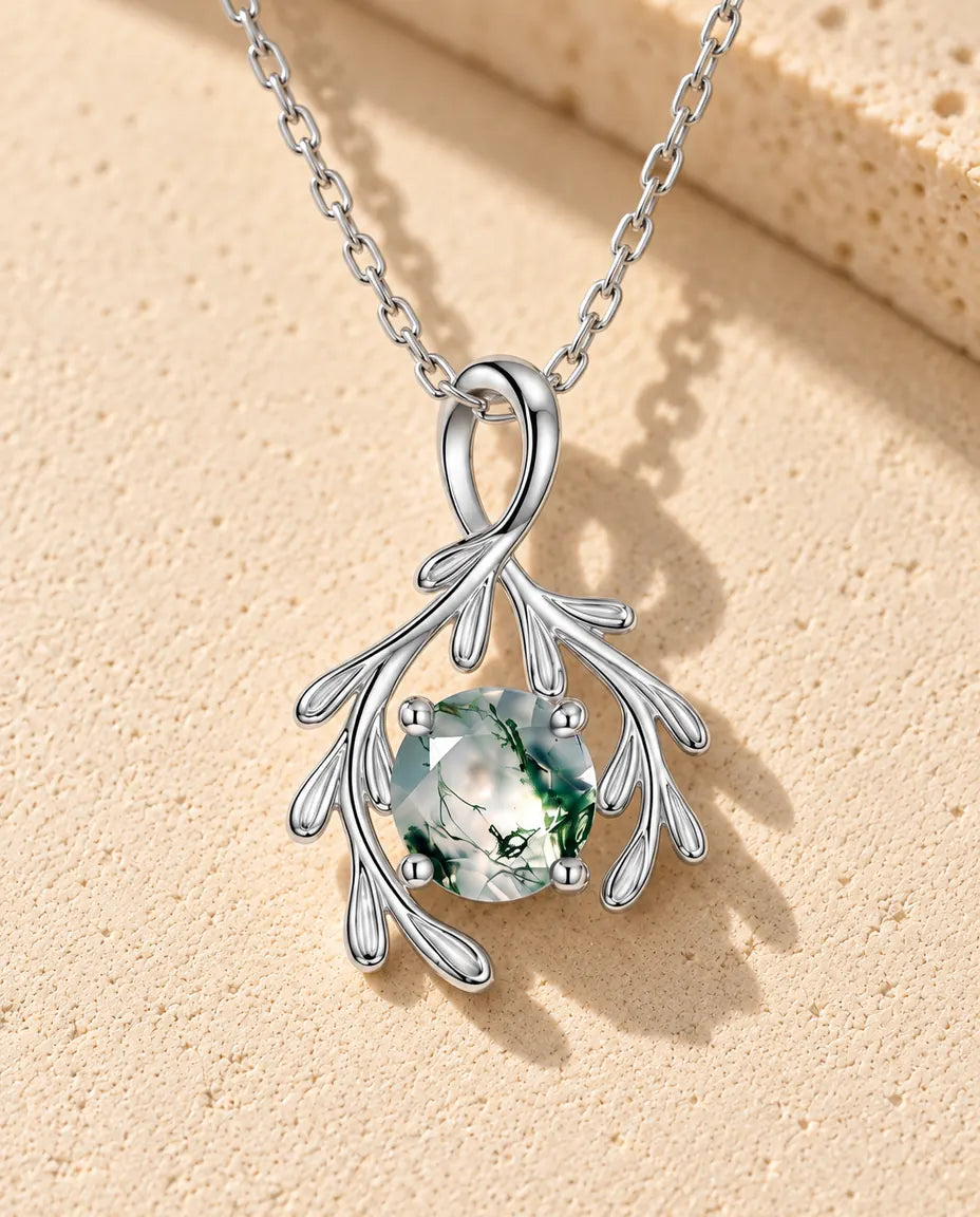 Moss Agate Branch Necklace in 925 Sterling Silver - lying on a cream textured surface beside a travertine block