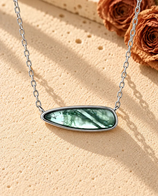 Moss Agate Bar Necklace in 925 Sterling Silver - lying on a cream textured surface beside a travertine block
