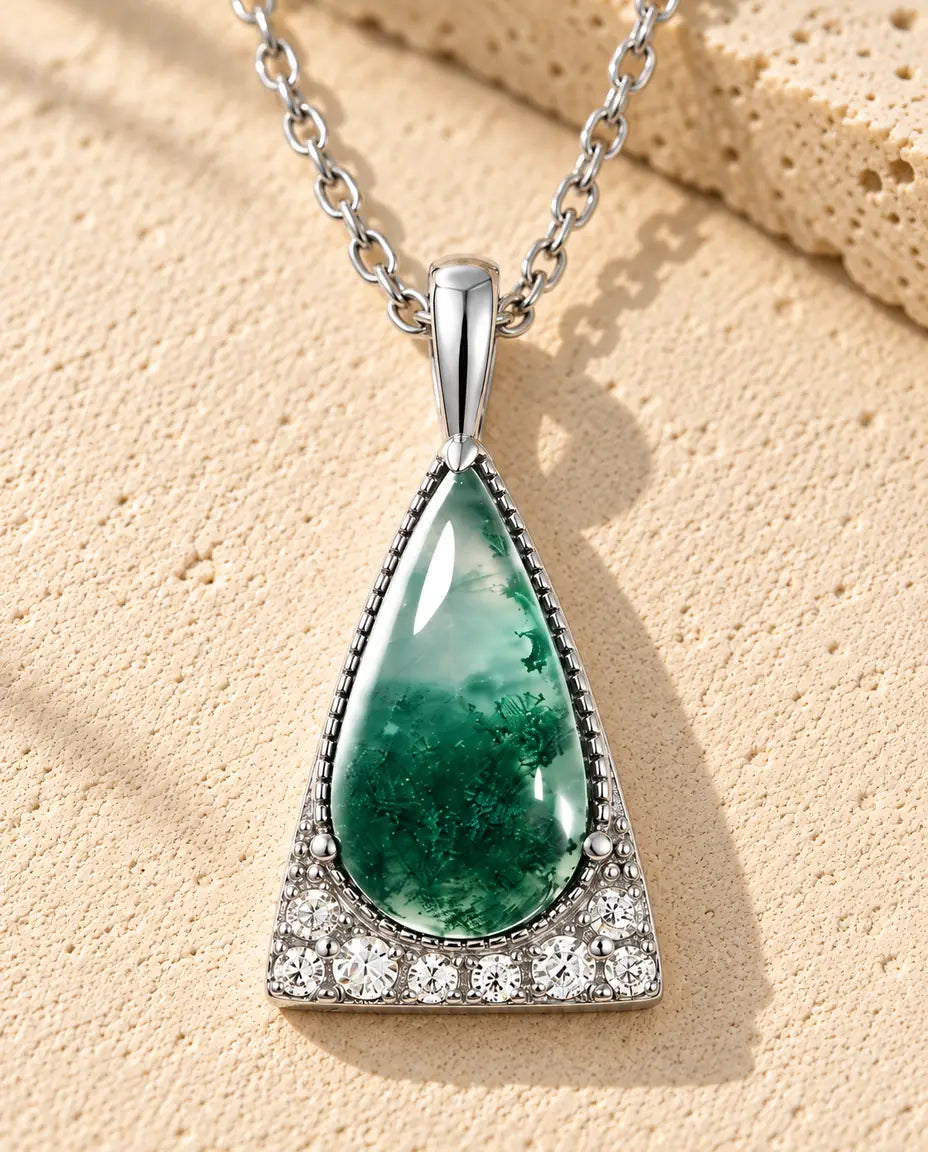 Moss Agate Triangle Necklace in 925 Sterling Silver - lying on a cream textured surface beside a travertine block
