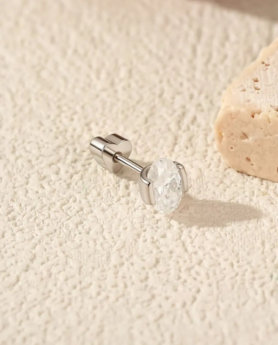Oval Moissanite Stud Earrings in 925 Sterling Silver - lying on its side on a cream textured surface, heart-shaped back on the post