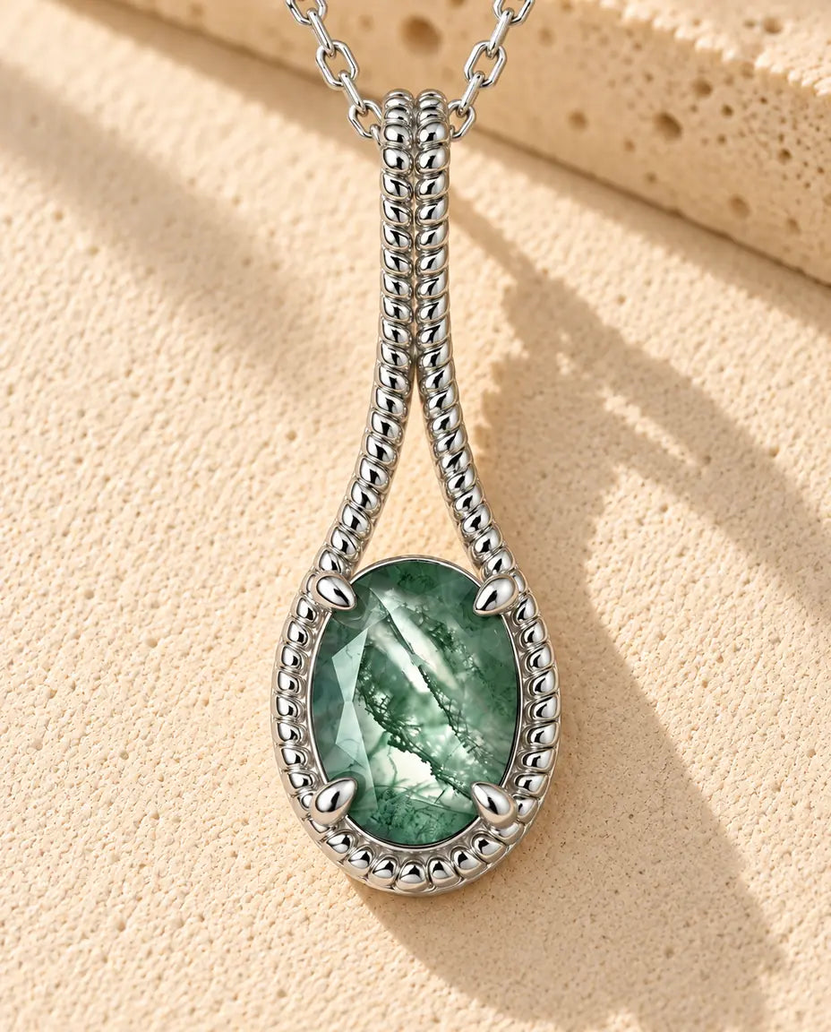 Oval Moss Agate Drop Necklace in 925 Sterling Silver - lying on a cream textured surface beside a travertine block