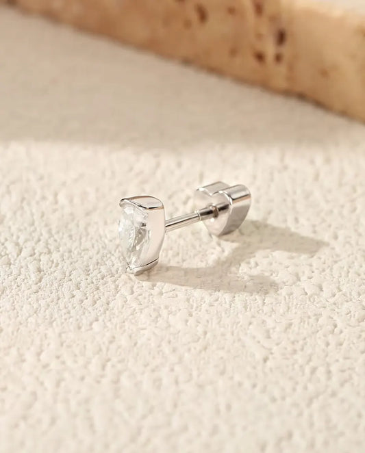 Pear Moissanite Stud Earrings in 925 Sterling Silver - lying on a cream textured surface beside a travertine slab