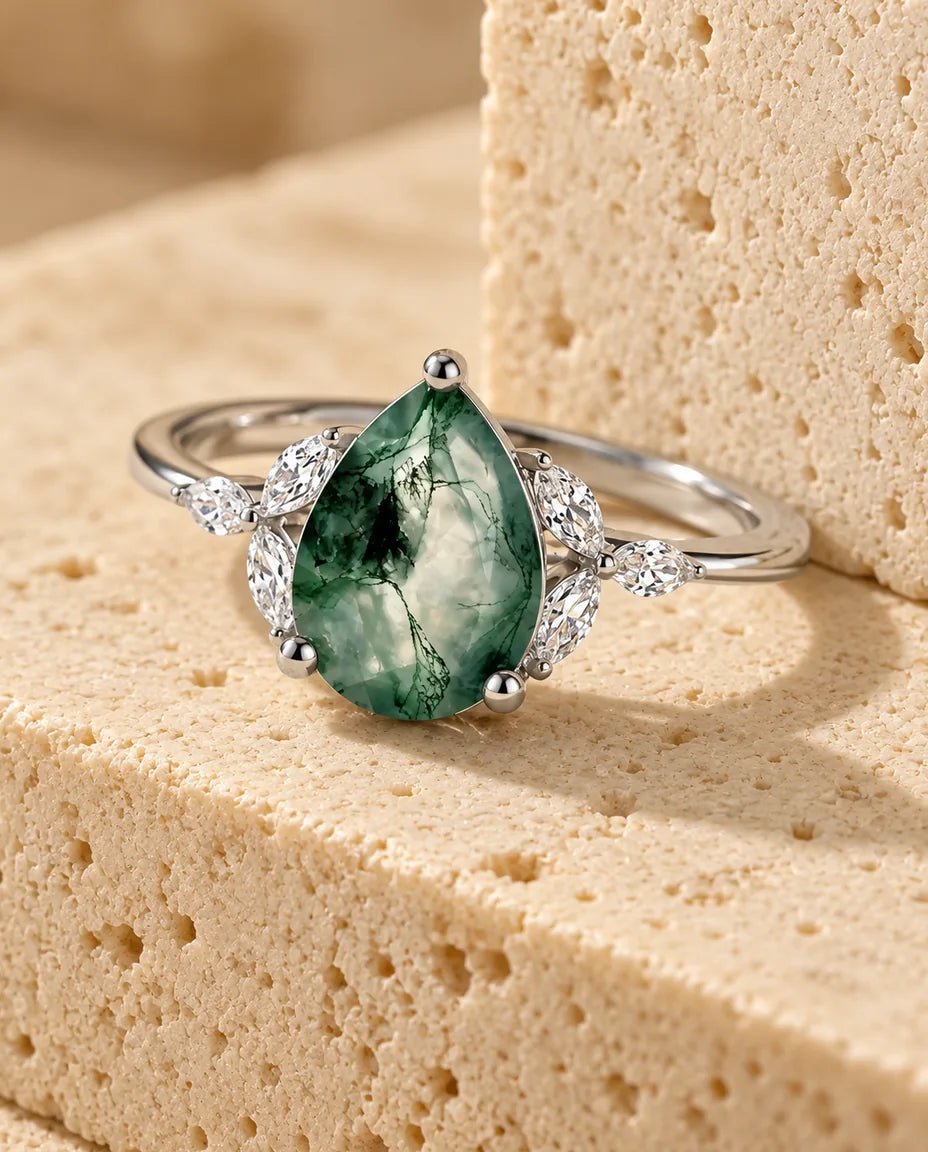 Pear-Shaped Moss Agate Engagement Ring - displayed on a travertine block
