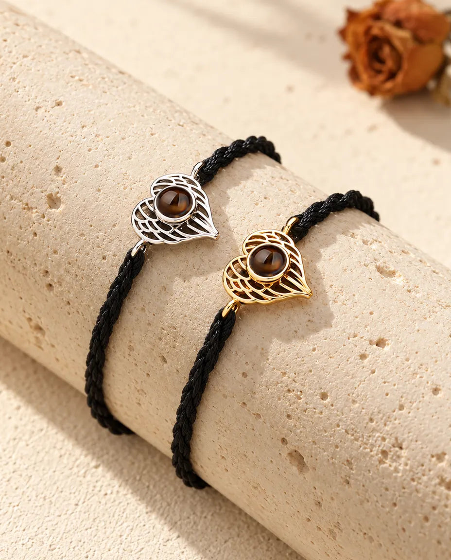 Silver tone and gold tone angel wing heart bracelets side by side on a travertine block