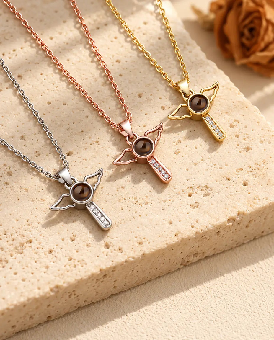 Three angel wings cross necklaces laid diagonally beside travertine