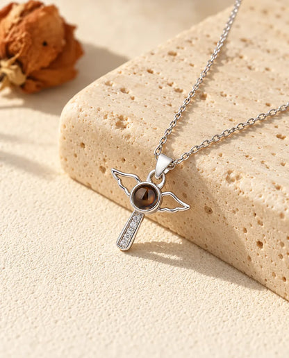 Silver tone angel wings cross with a cubic zirconia stem on travertine
