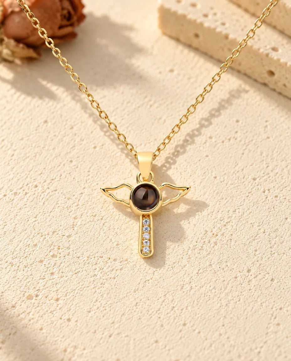 Front view of the gold tone cross with open angel wings and the projection stone at its centre