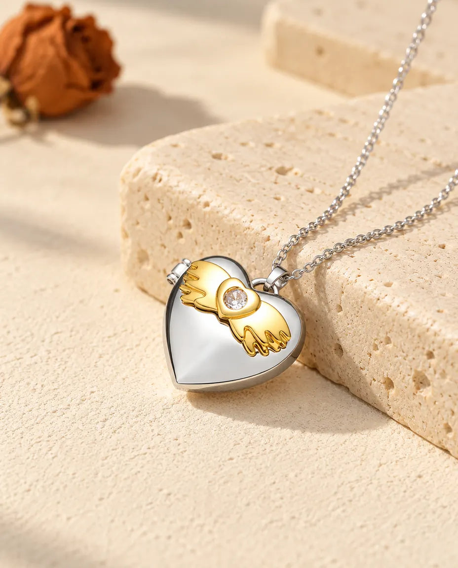 Personalised angel wings heart photo locket necklace in silver tone with gold tone angel wings, resting on a travertine block