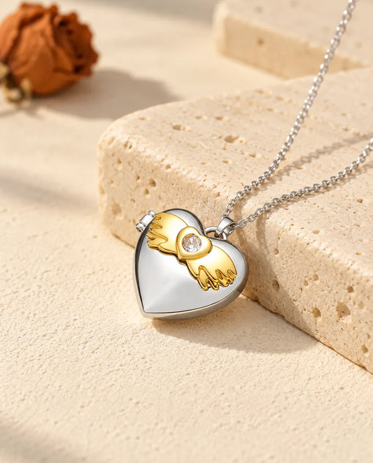 Personalised angel wings heart photo locket necklace in silver tone with gold tone angel wings, resting on a travertine block