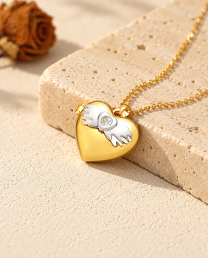 Gold tone angel wings heart photo locket necklace resting on a travertine block