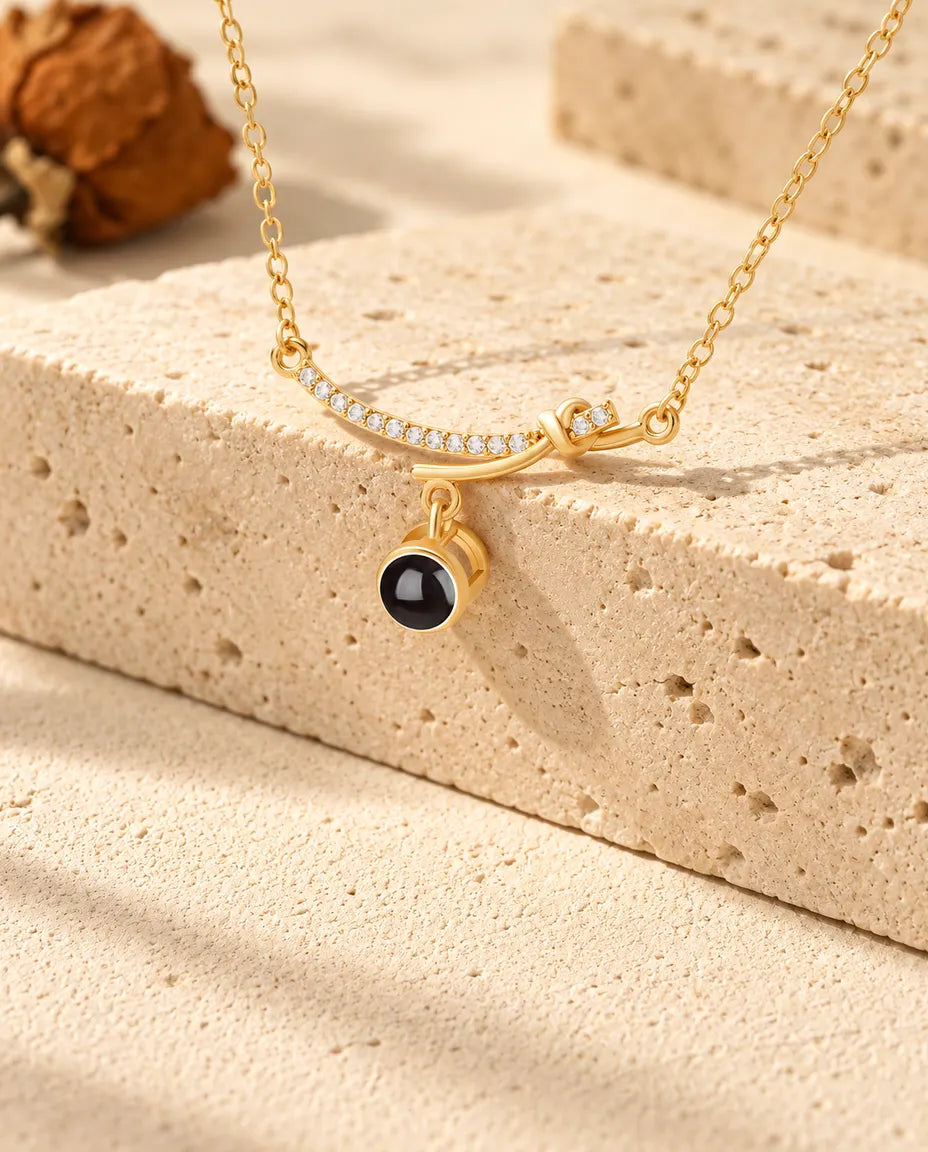 Personalised gold tone curved bar photo projection necklace draped over a travertine block