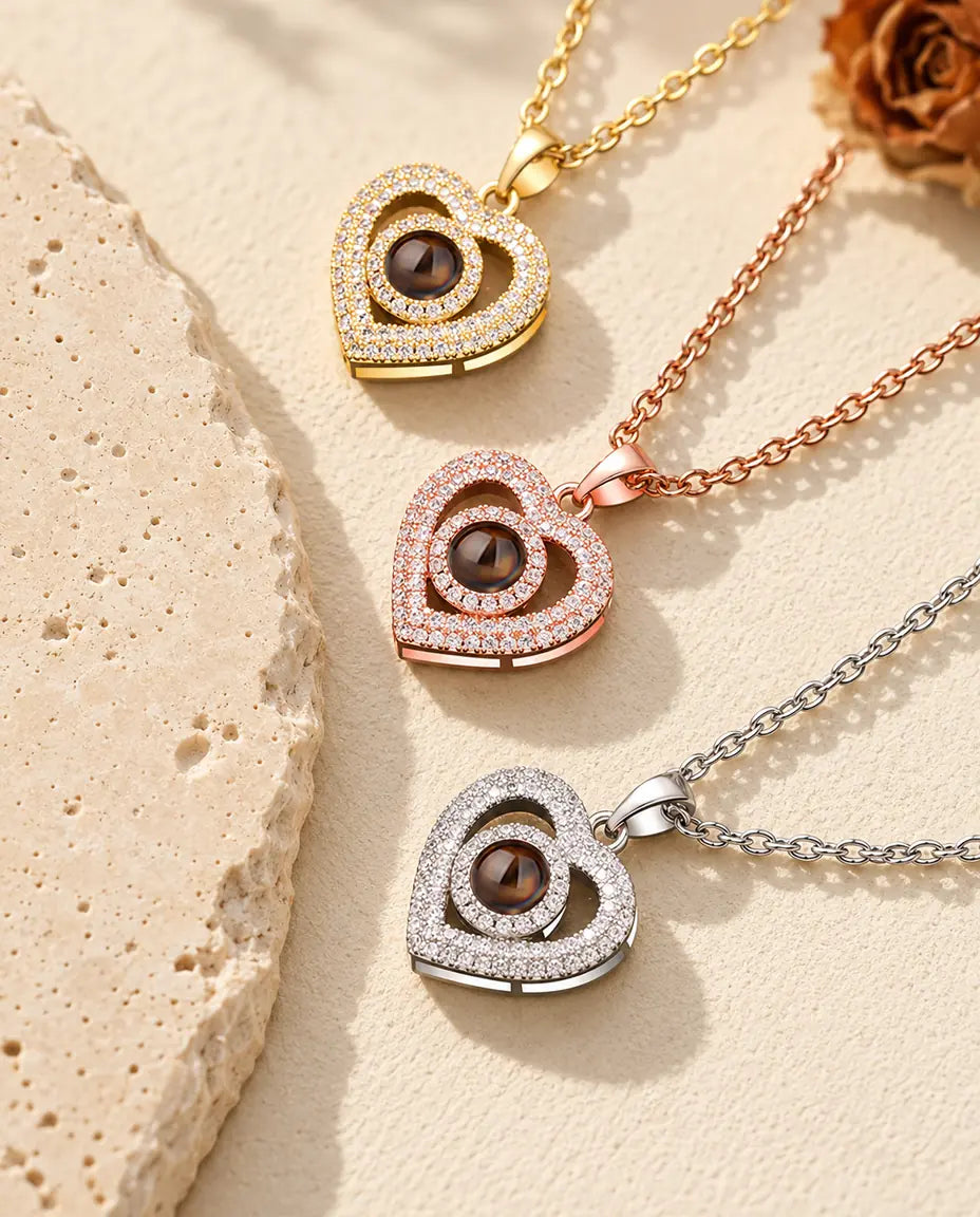 Gold tone, rose gold tone and silver tone double heart pendants stacked beside a travertine slab