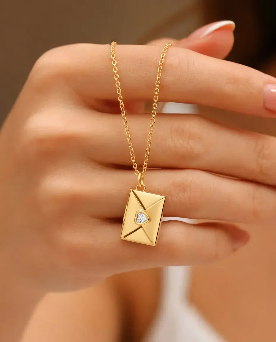 Gold envelope photo locket necklace with heart stone held in hand