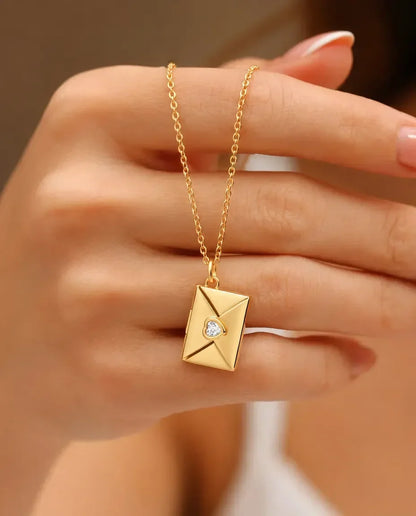Gold envelope photo locket necklace with heart stone held in hand