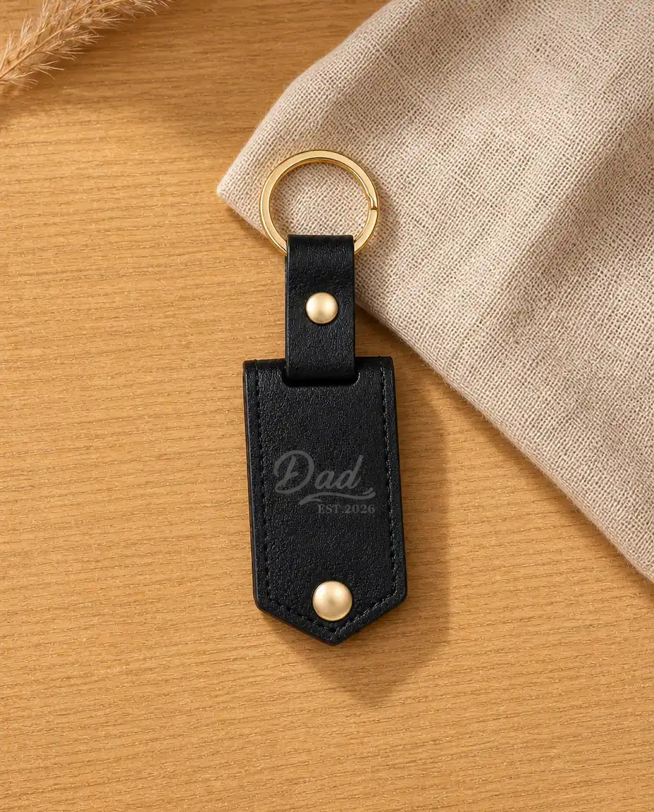Personalised black faux leather photo keyring engraved with Dad Est. 2026 on a warm wood table