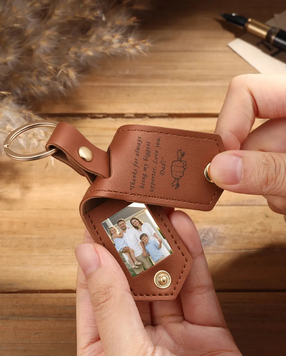 Hands holding an open brown faux leather photo keyring with two family photos