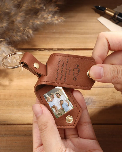 Hands holding an open brown faux leather photo keyring with two family photos
