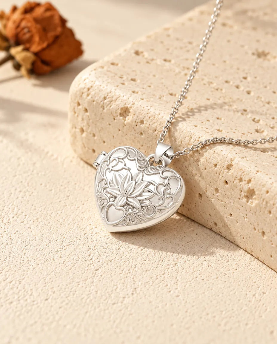 Personalised lotus flower heart photo locket necklace in silver tone with embossed scrollwork, resting on a travertine block