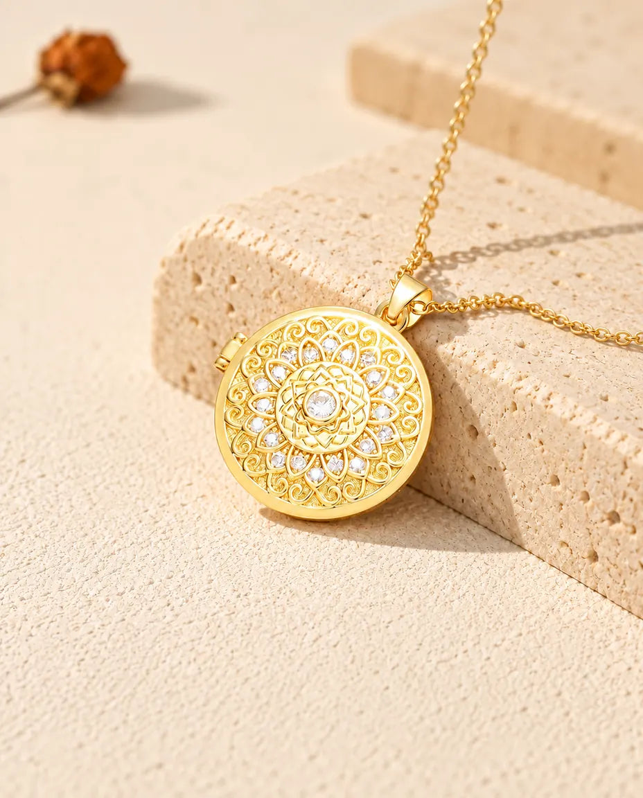 Gold tone mandala flower photo locket necklace resting on a travertine block