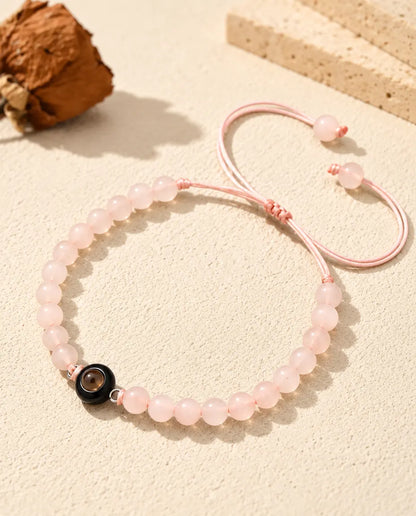 Rose pink bead bracelet with a black projection ring charm on cream plaster