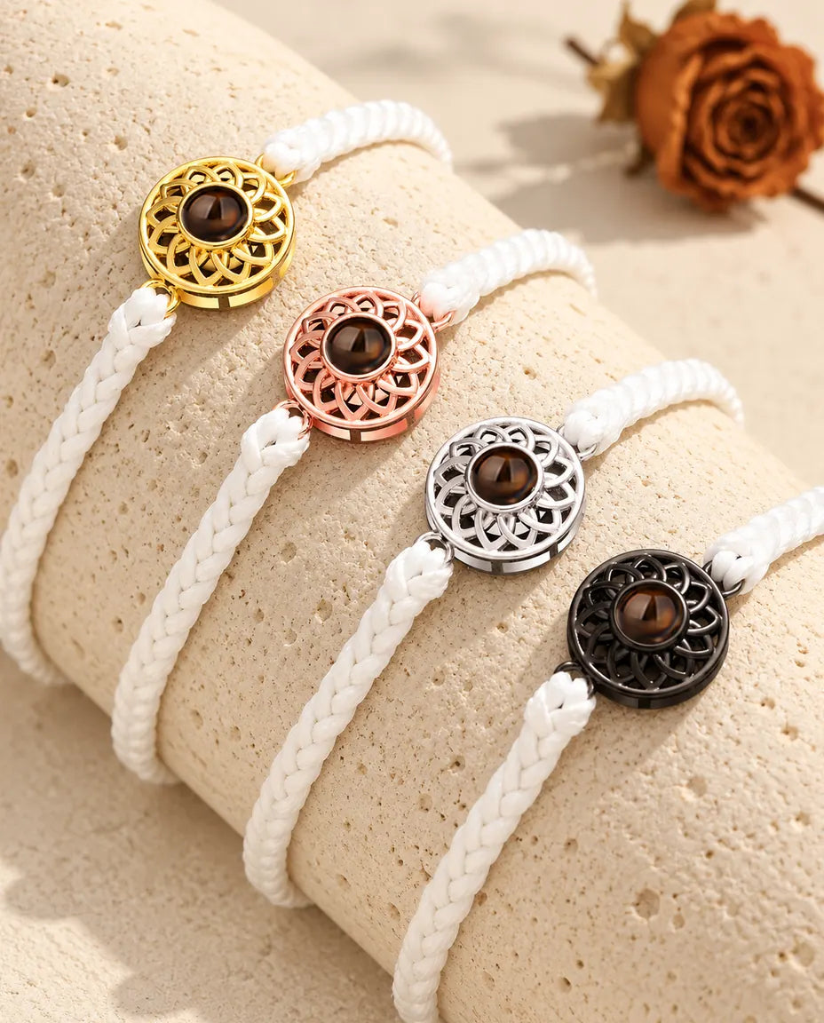 Four white thin braided cord bracelets with gold tone, rose gold tone, silver tone and black round charms on a travertine block