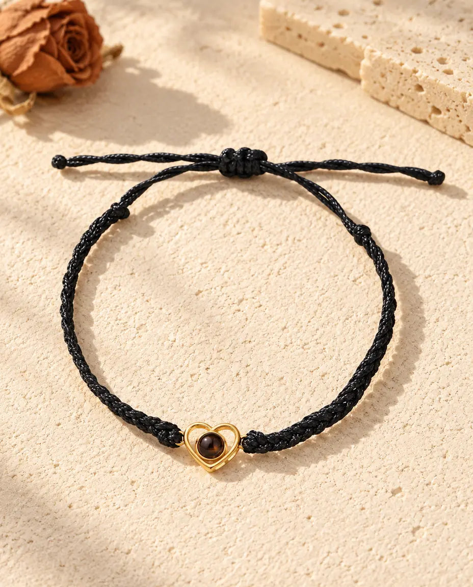Top view of the gold tone open heart bracelet on a black braided cord with its sliding knot