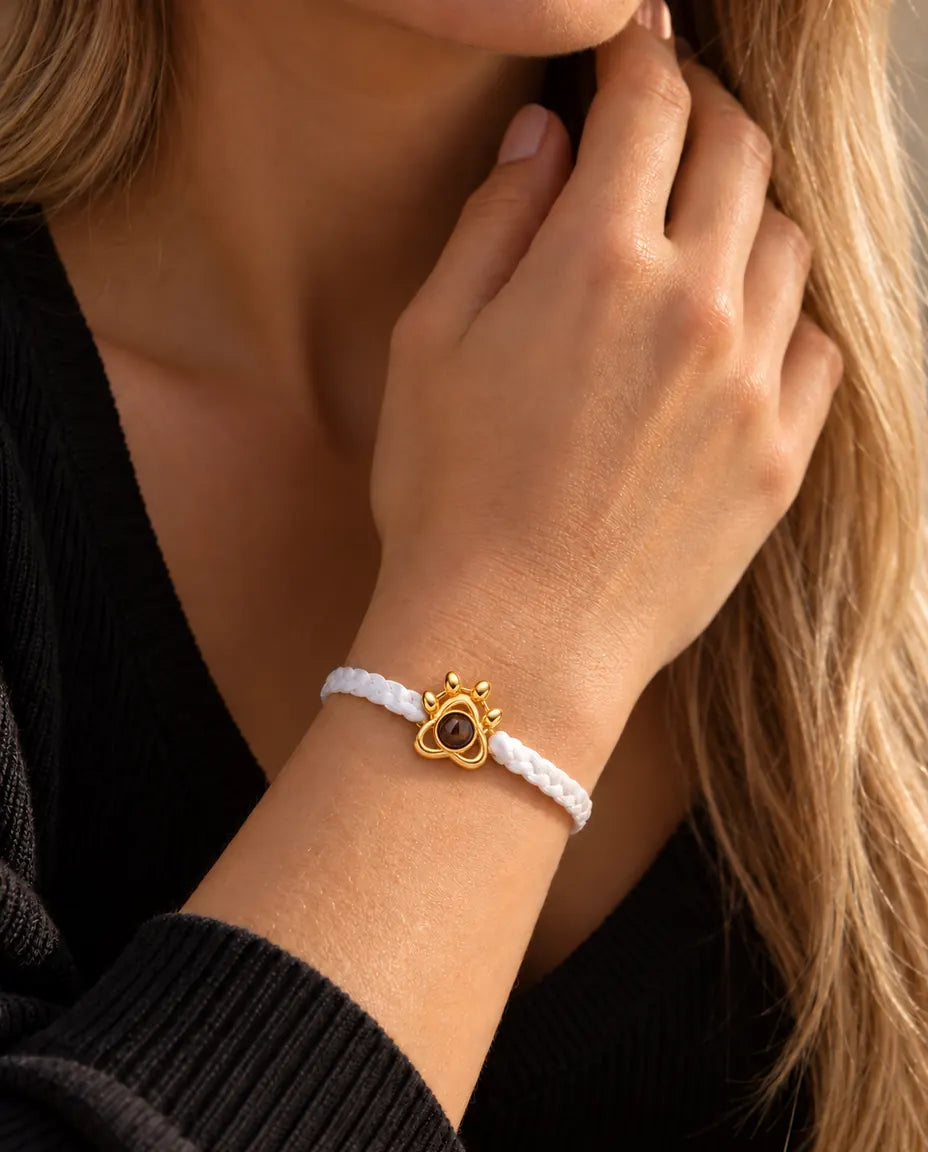 Close-up of the gold tone paw charm on a white braided cord, worn on the wrist near the neck